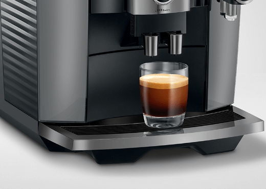 Ekspres z czarną obudową oraz z filiżanką kawy espresso stojacą na niej