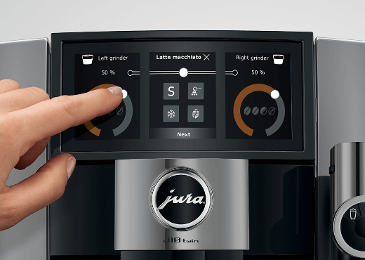 Ręka dotykająca ekranu dotykowego ekspresu do kawy, pokazującego opcje mielenia i przygotowania kawy